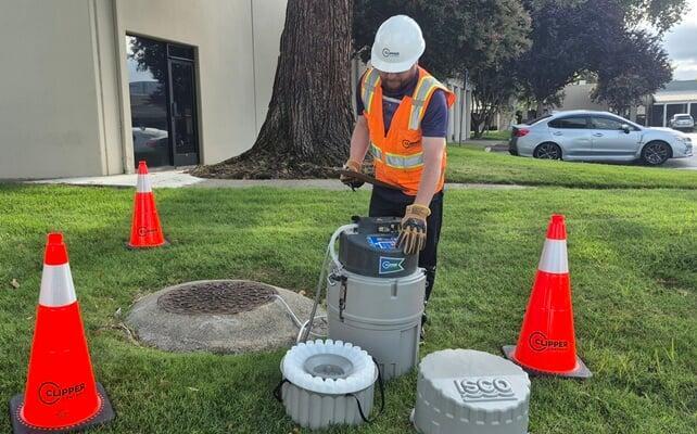 A field technician programming a portable sampler next to a manhole